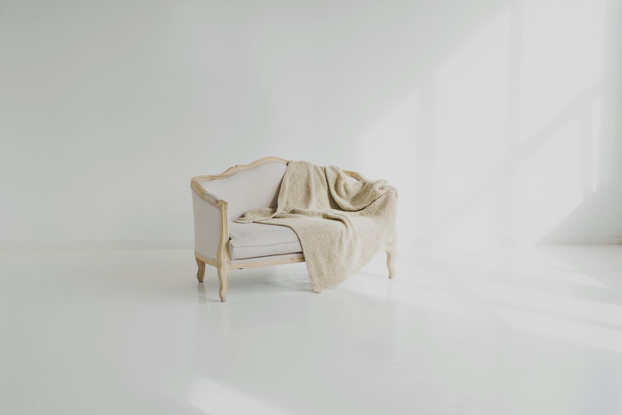 A beige throw on a vintage white sofa in a bright minimalist living space.